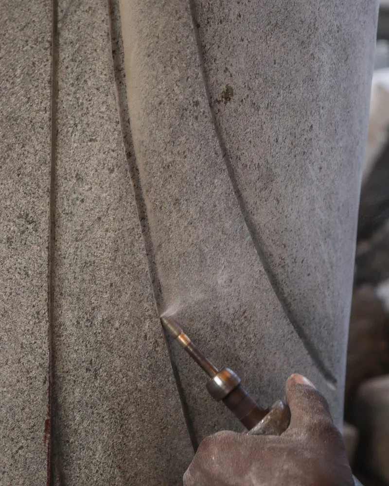 Cincel apoyado sobre una superficie de piedra gris levantando polvo mientras se abre un surco curvo